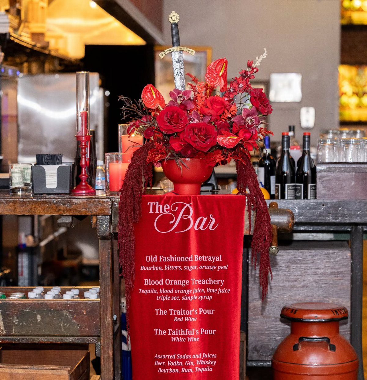 Themed bar setup with red flowers, a sword, and a betrayal-themed cocktail menu.