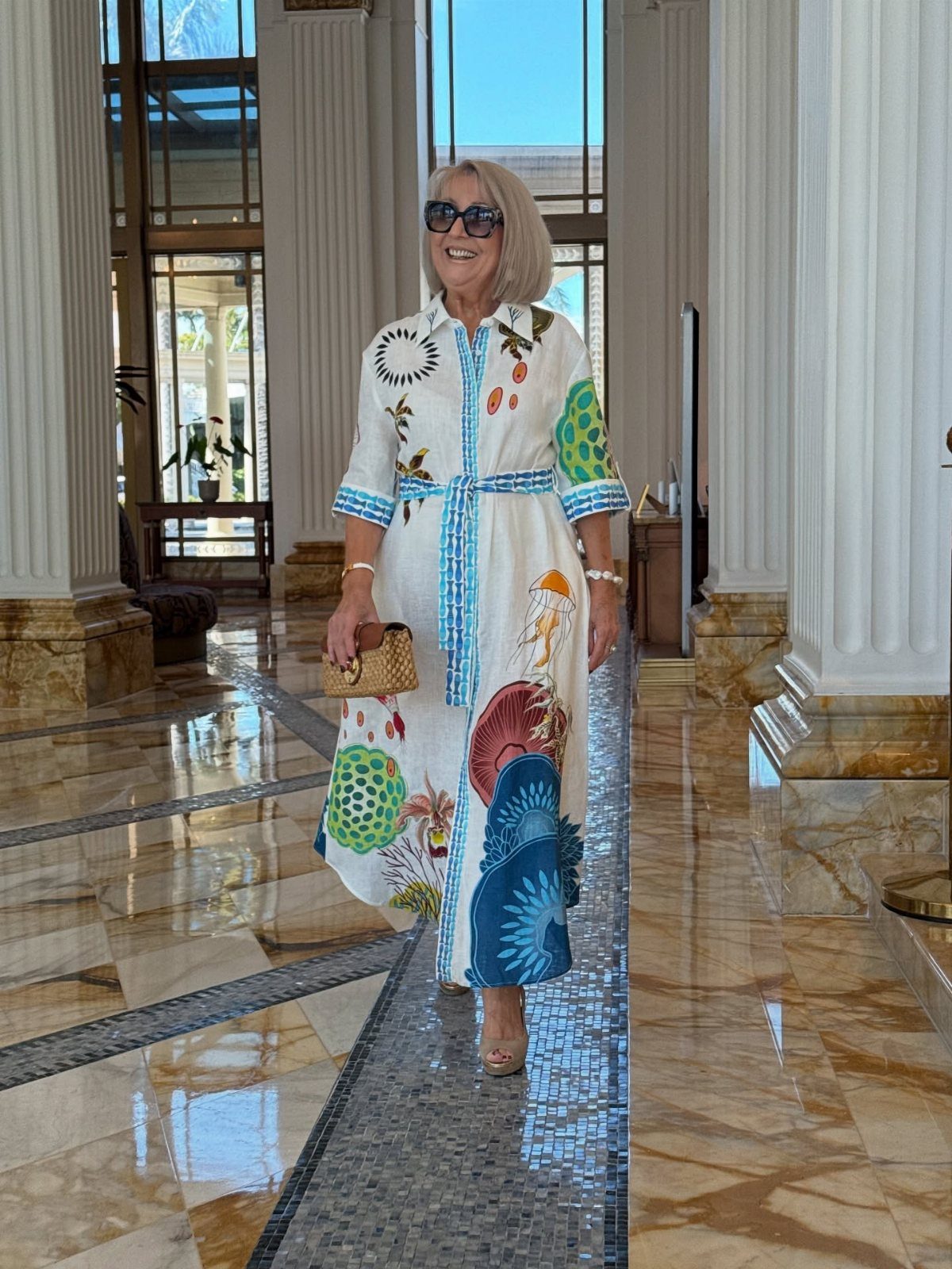 Woman wearing a white colorful patterned shirt dress walking in a marble hall.