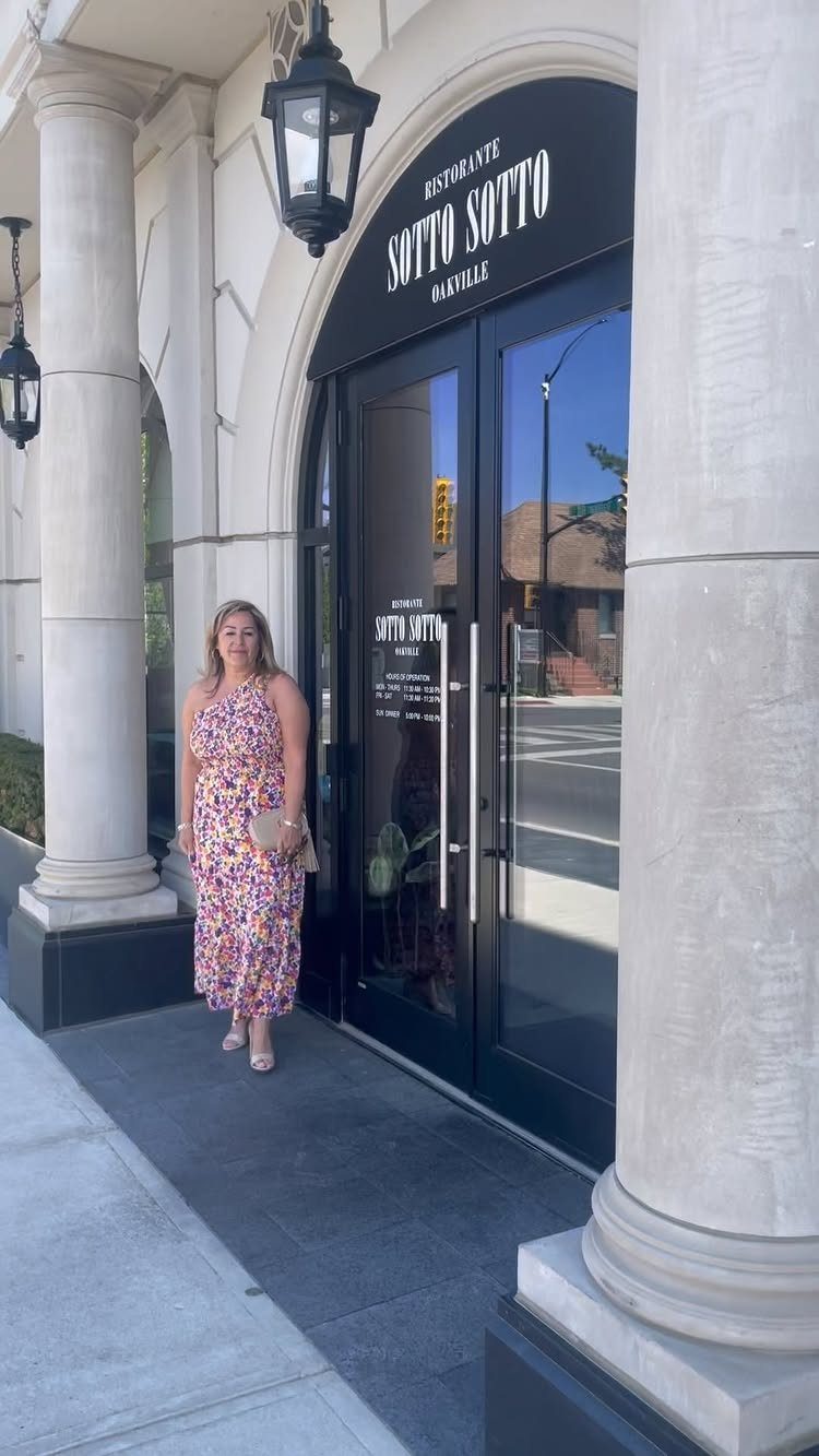 Woman in a colorful floral flowy midi dress standing before a restaurant entrance.
