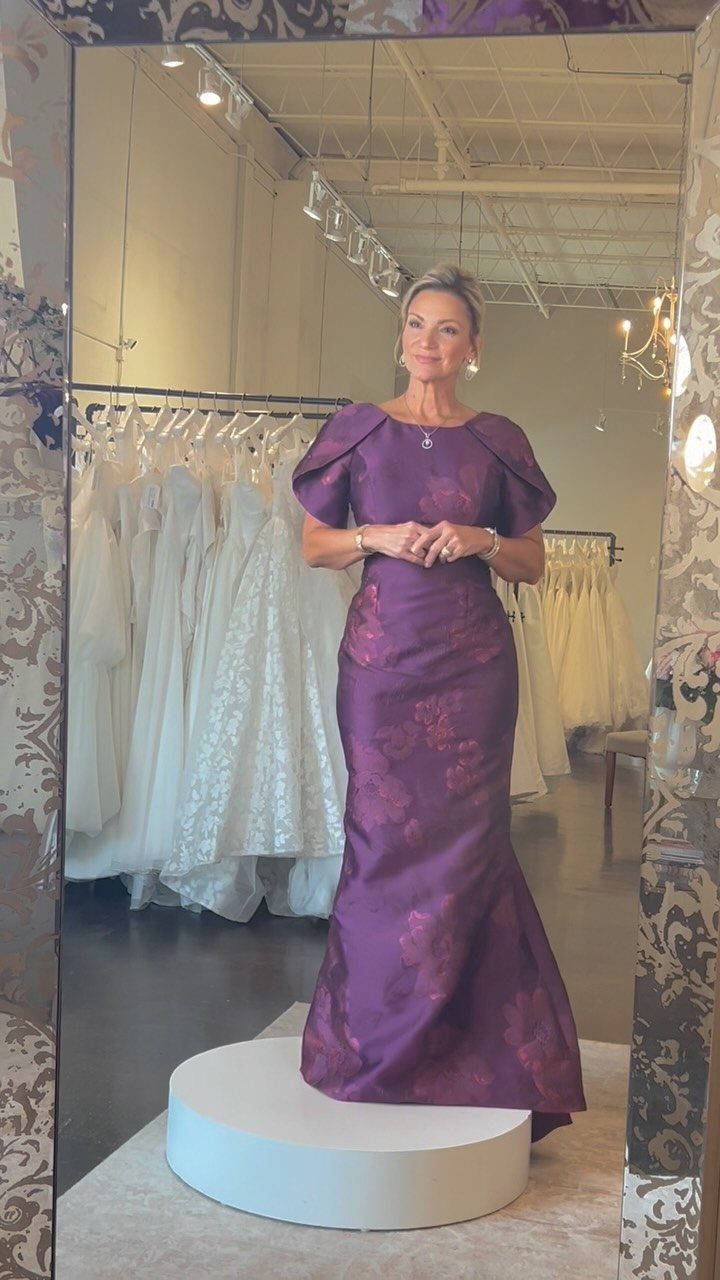 Woman wearing a floor-length purple satin gown standing on a white podium.