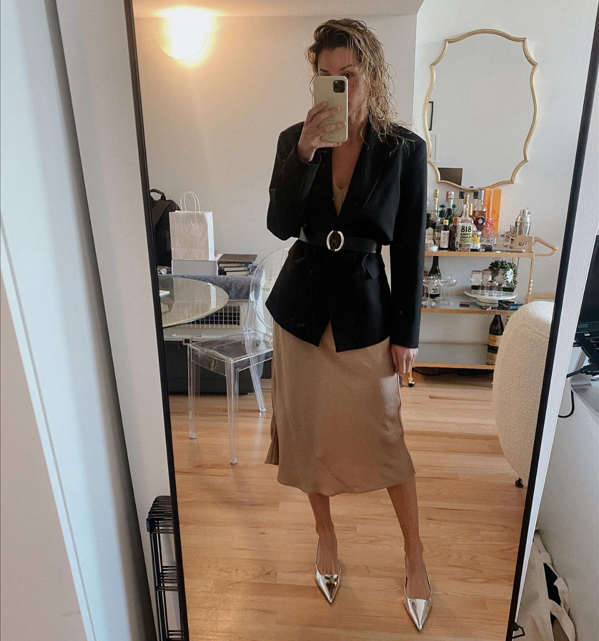 Woman wearing a black belted blazer over a champagne satin slip dress and heels.