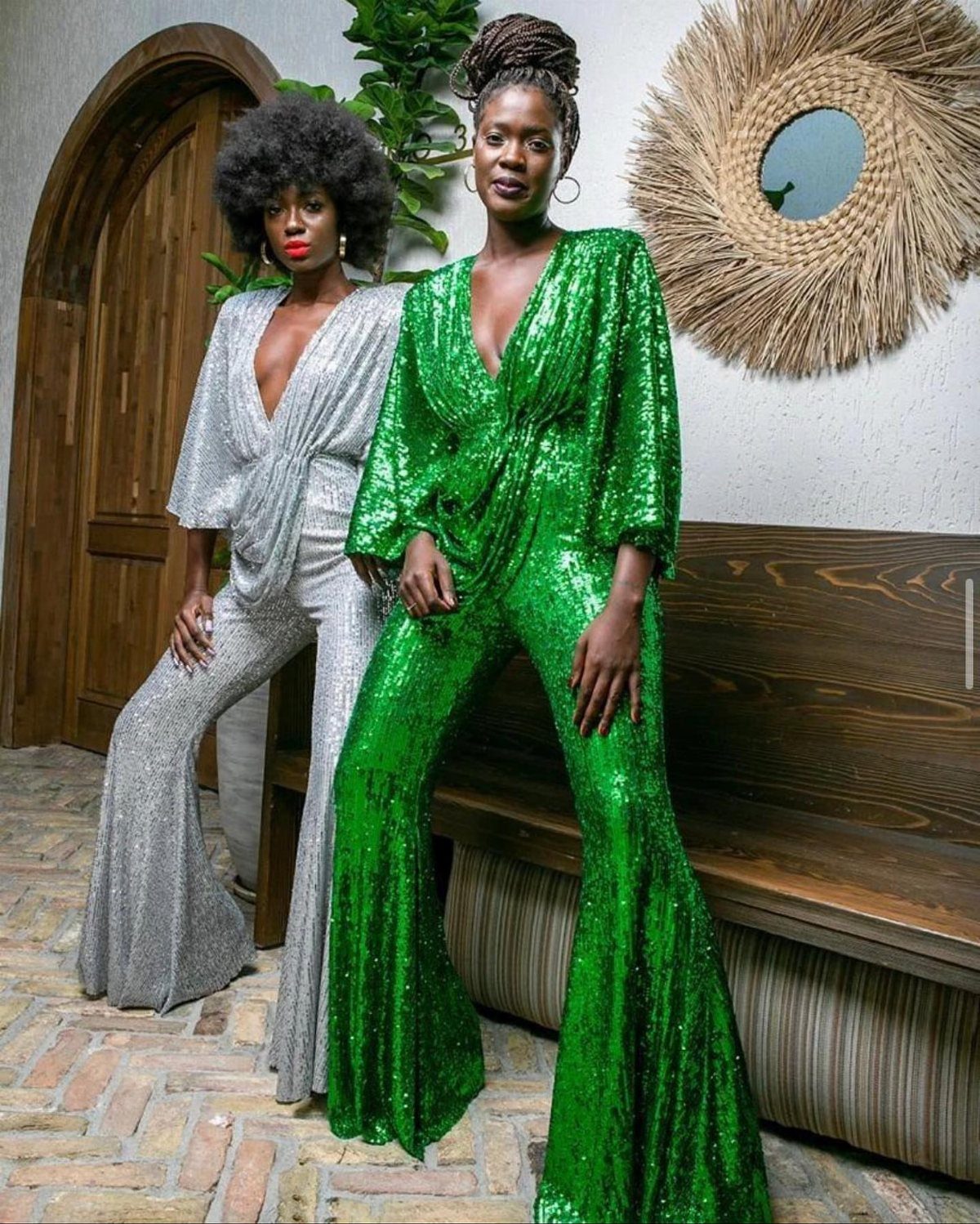 Two women wearing shimmering silver and green sequined jumpsuits with wide legs.
