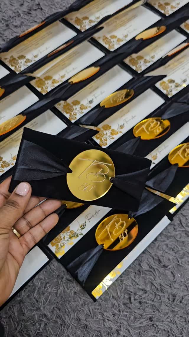 Black velvet invitation envelopes with gold seals and ribbons arranged on grey carpet.