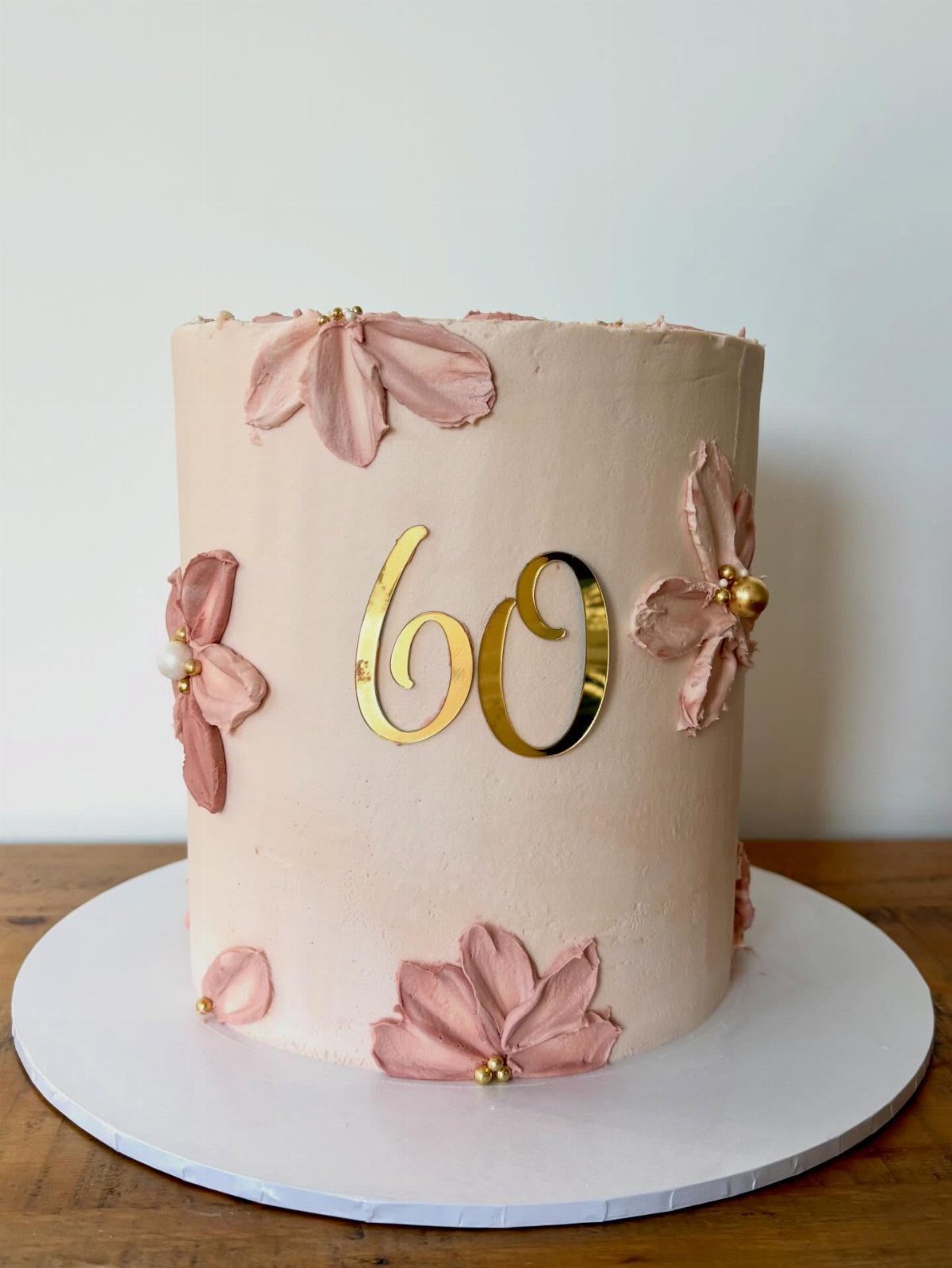 Pale pink birthday cake with gold number 60 and pink frosting flowers.