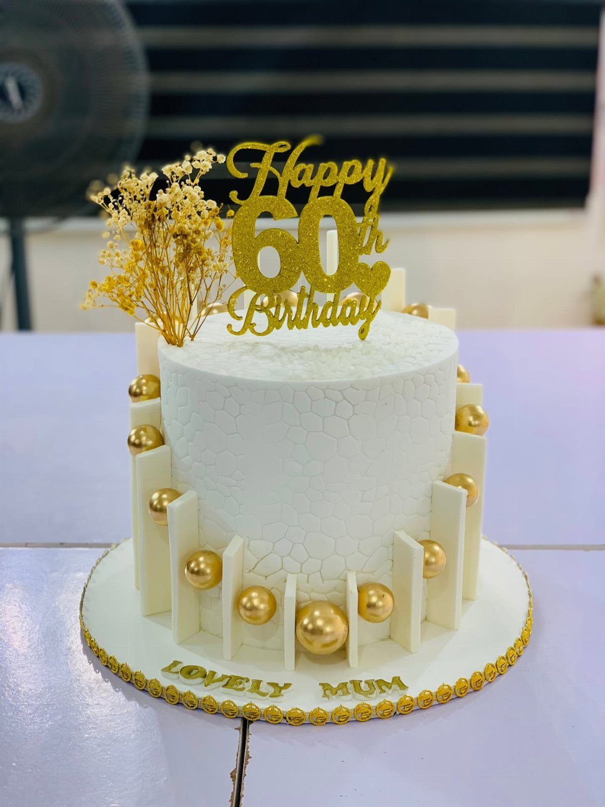 White 60th birthday cake for mum with gold spheres and birthday topper.