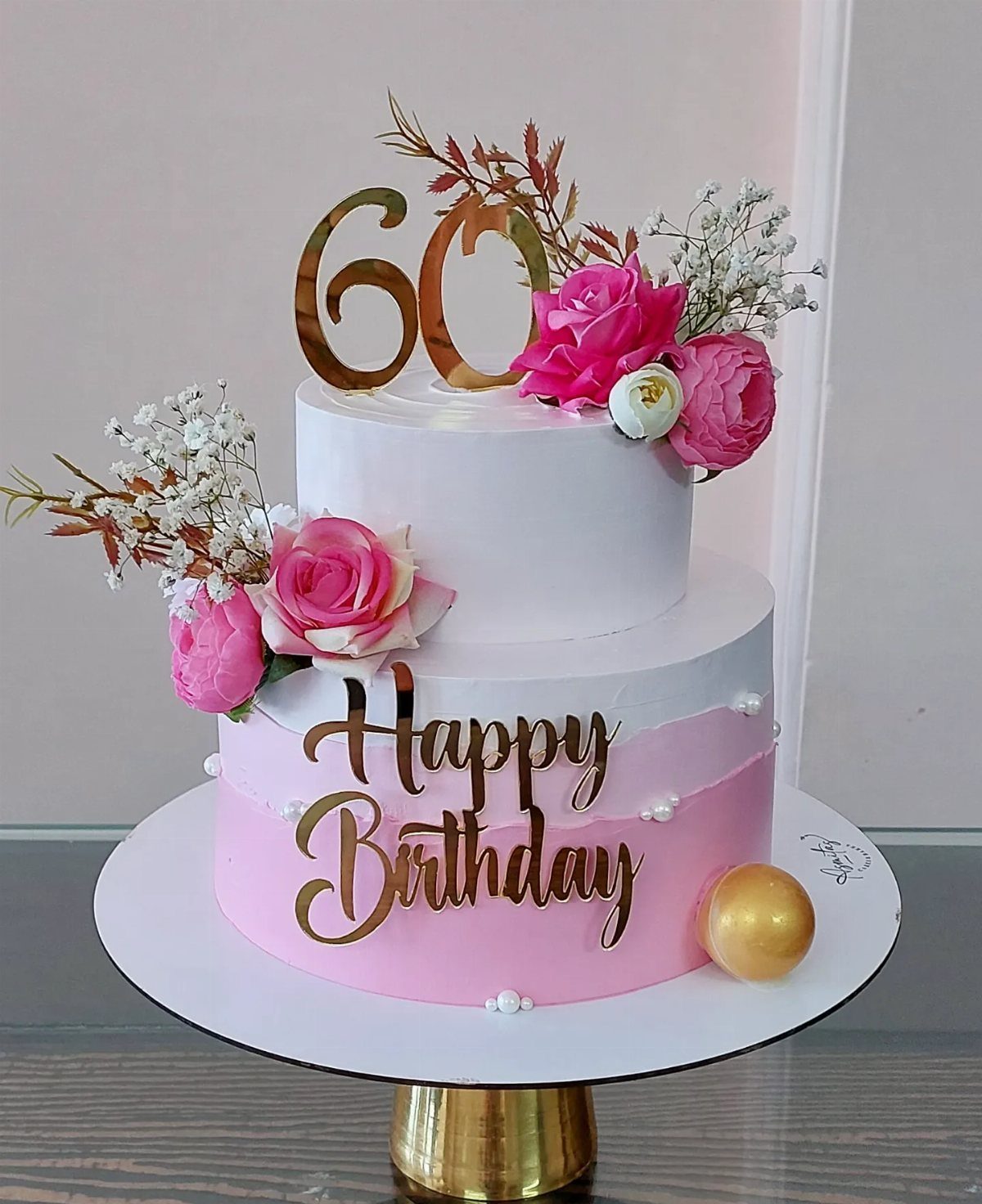 Two-tier white and pink birthday cake with gold 60 topper and pink roses