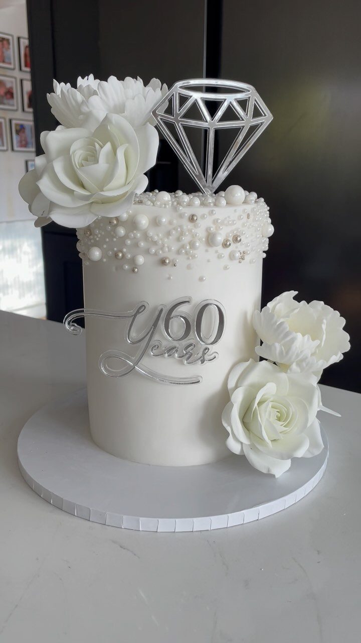 White frosted cake with sugar roses, edible pearls, and a silver 60 years topper.
