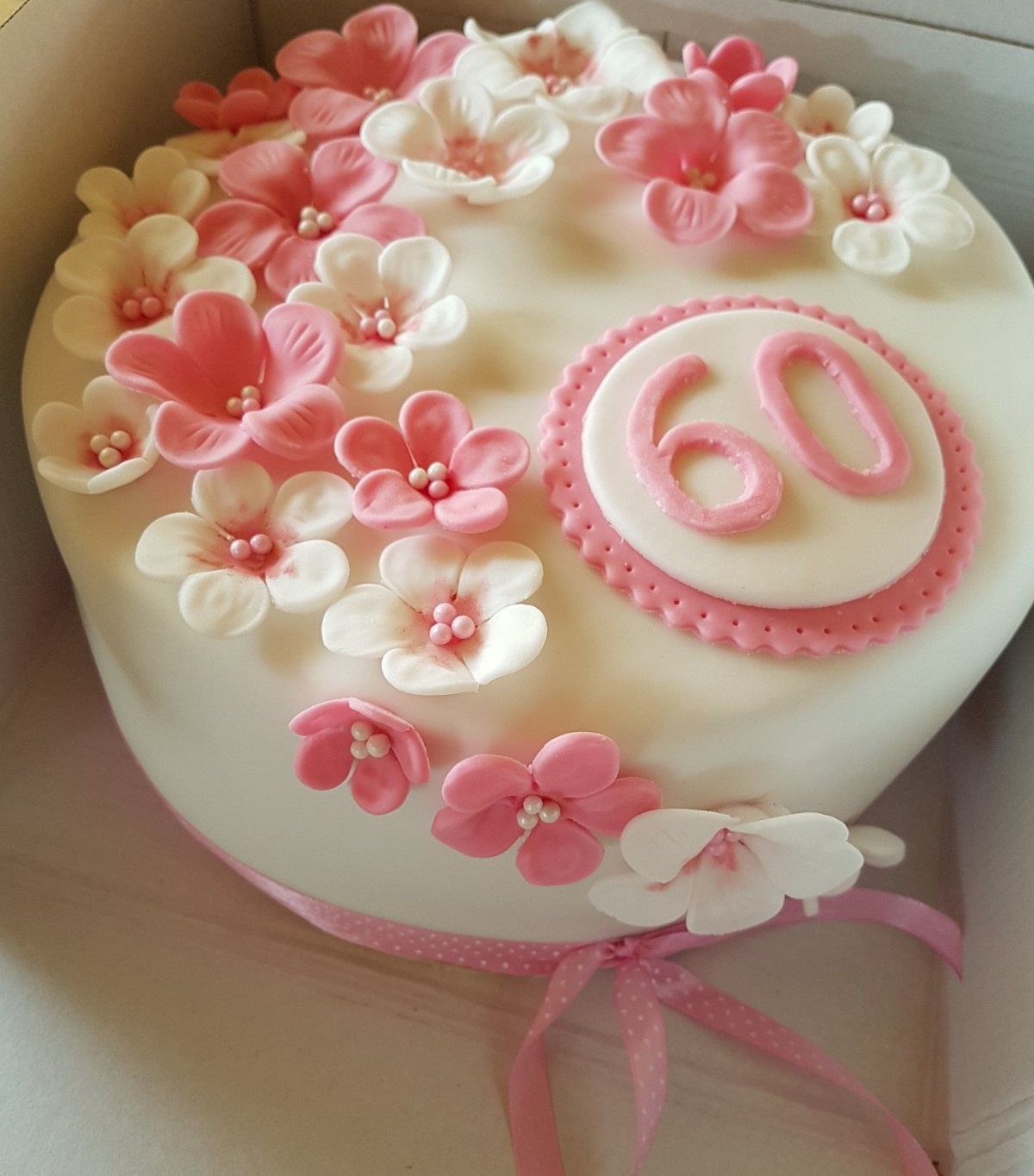 White fondant cake with pink and white sugar flowers and a pink 60 topper