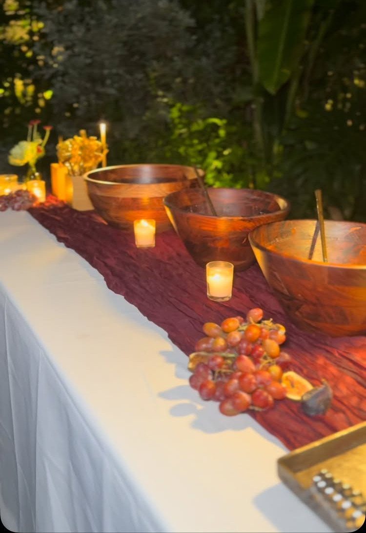 Wooden bowls and lit candles on a table with burgundy runner and grapes.