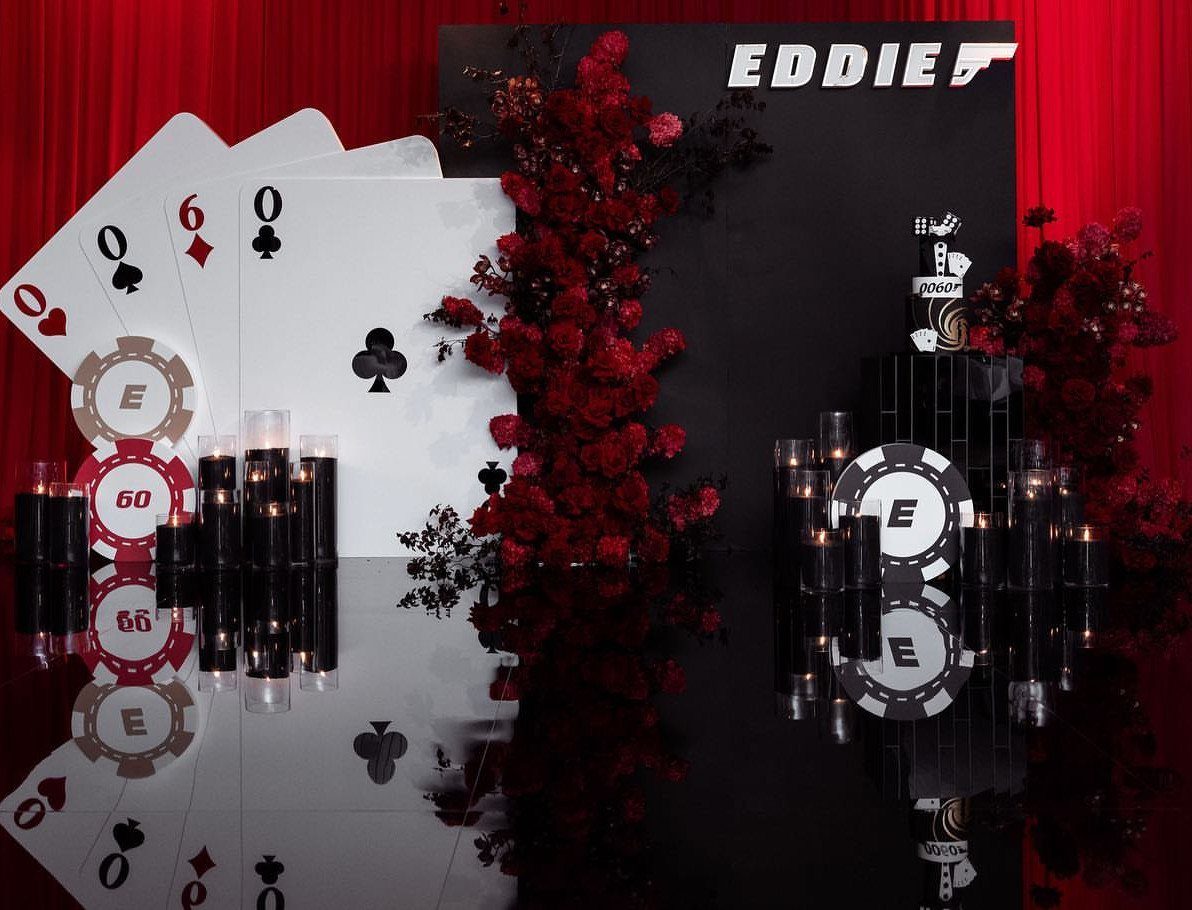 Casino themed birthday decorations with giant playing cards, chips, and red flowers.