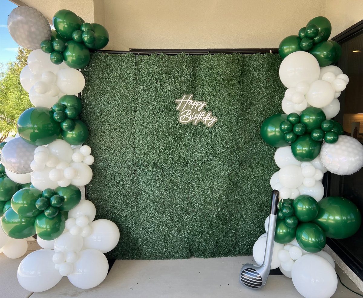 Green grass wall backdrop with white and green balloons and a golf club.
