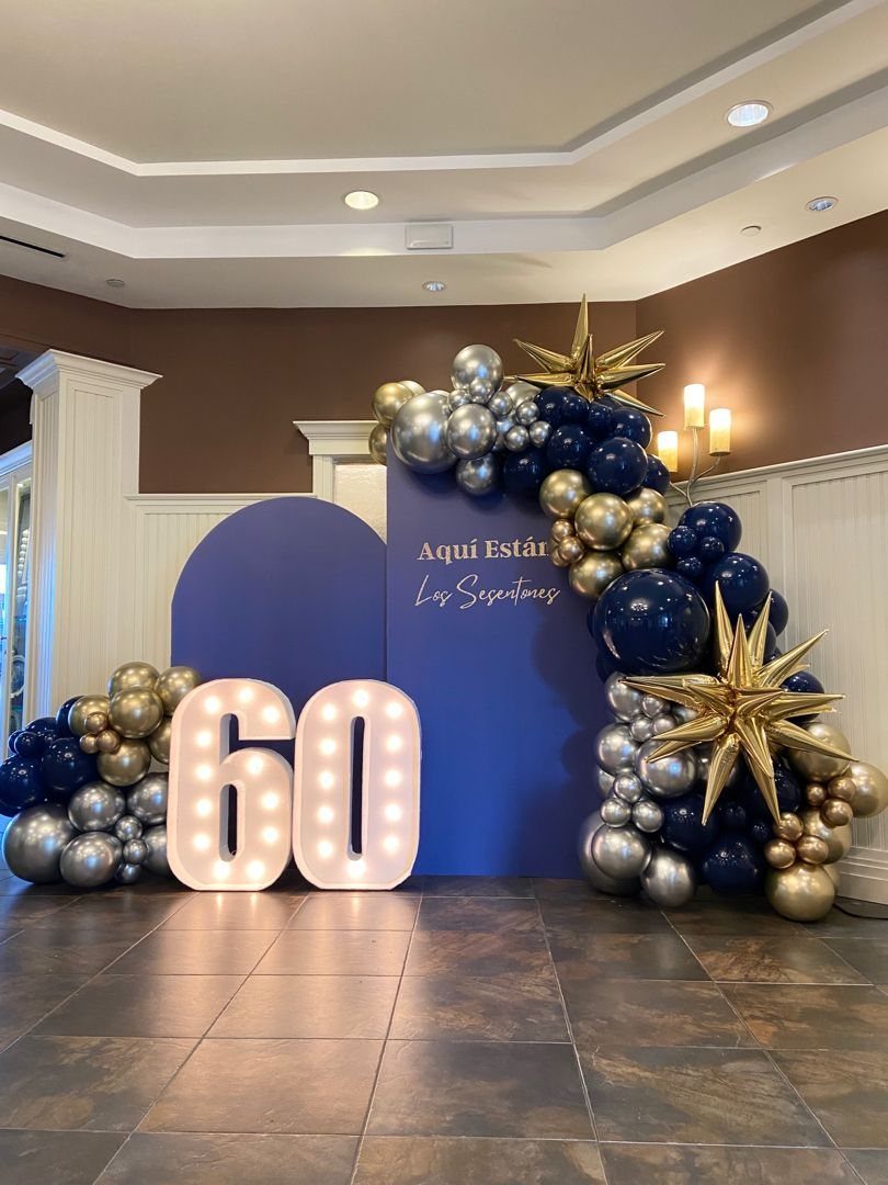Large illuminated 60 numbers with blue, gold, and silver balloon arch backdrop.