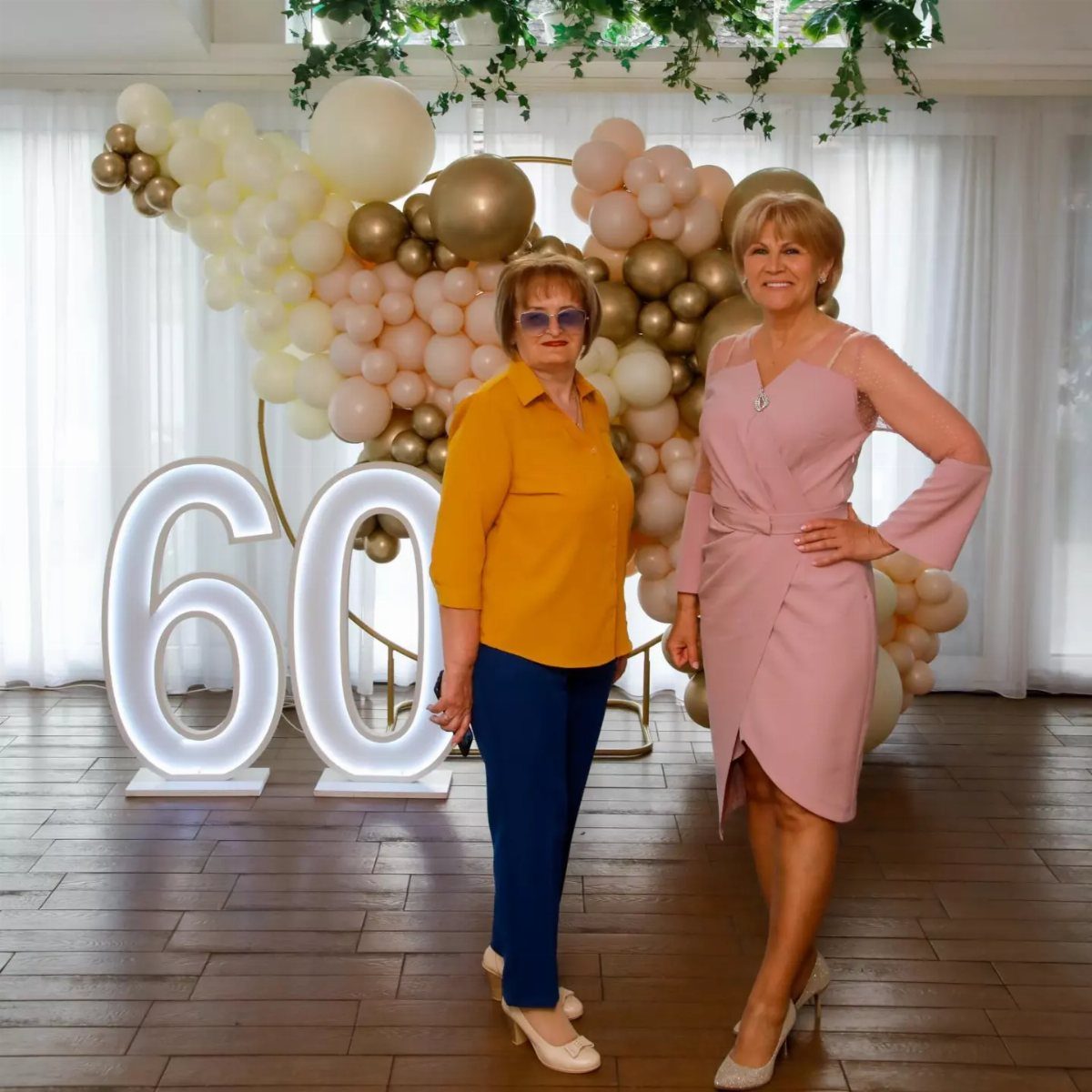 Two women posing by a 60th birthday balloon arch and illuminated numbers.