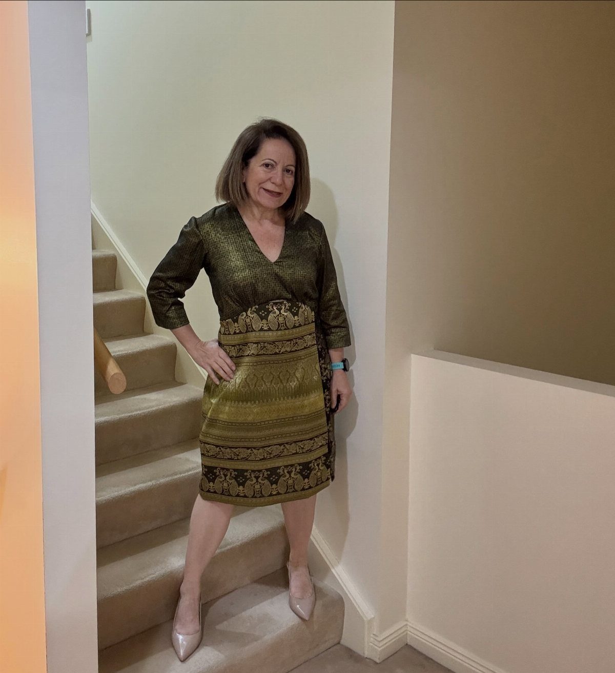 Woman in an olive-green and gold patterned knee-length dress posing on stairs