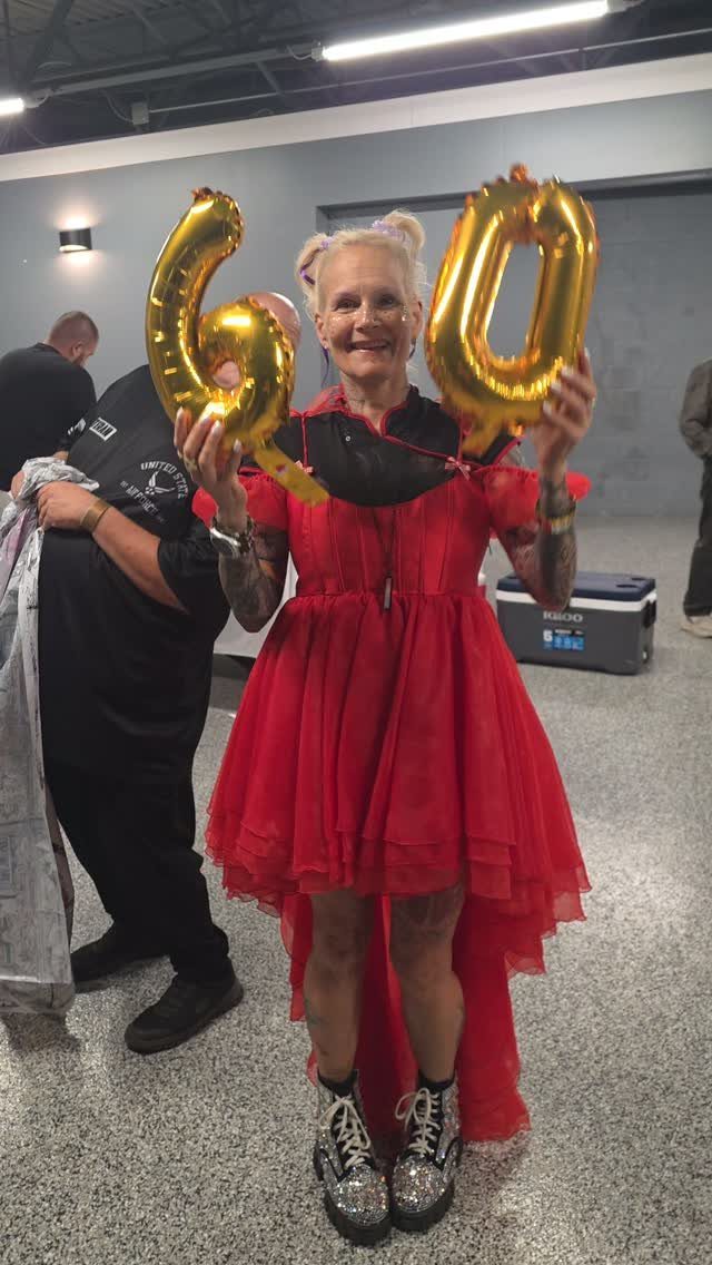 Woman in a red high-low dress holding gold 60 balloons and wearing silver boots.