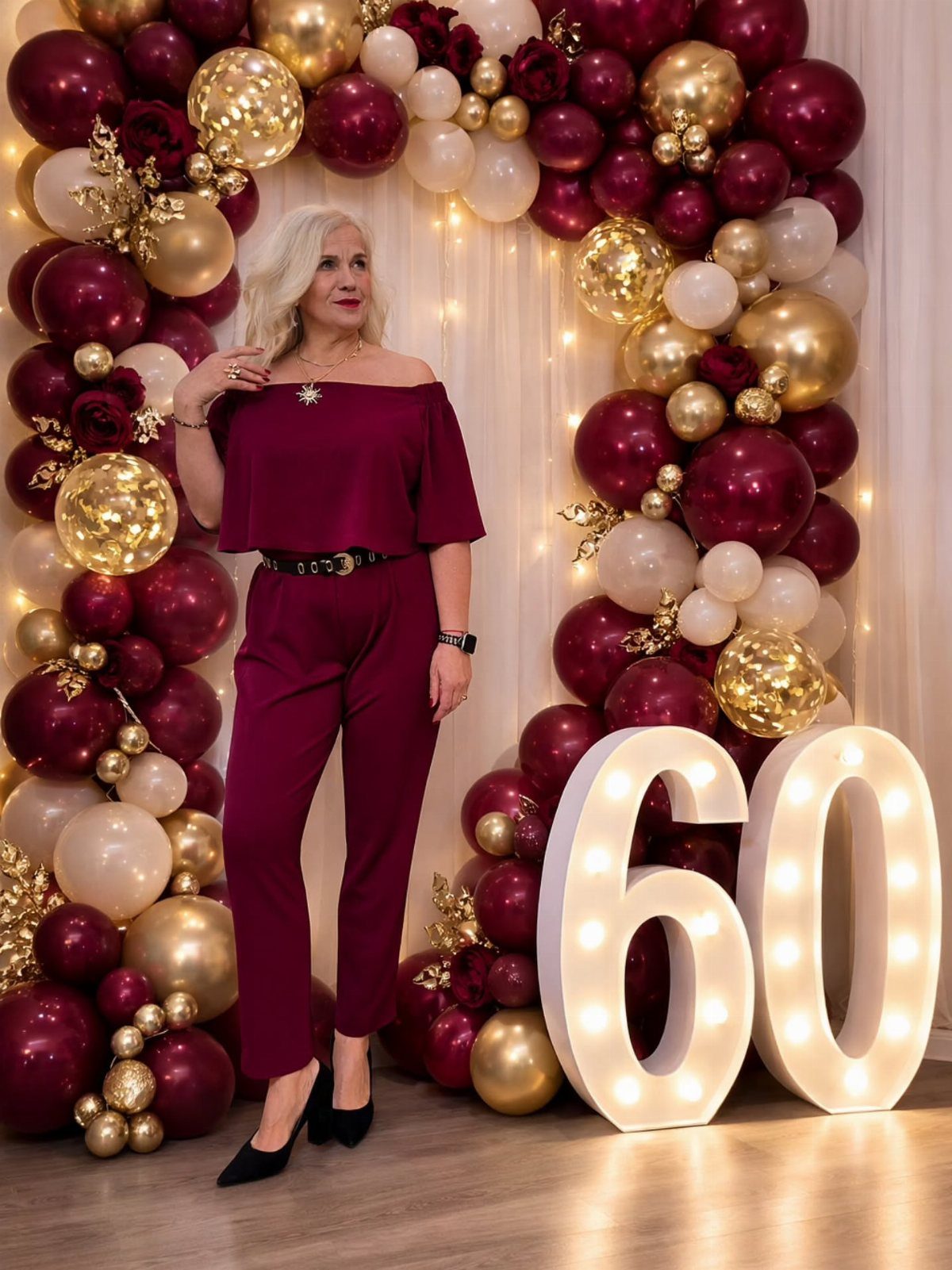 Woman in maroon jumpsuit posing by 60th birthday balloons and light-up numbers