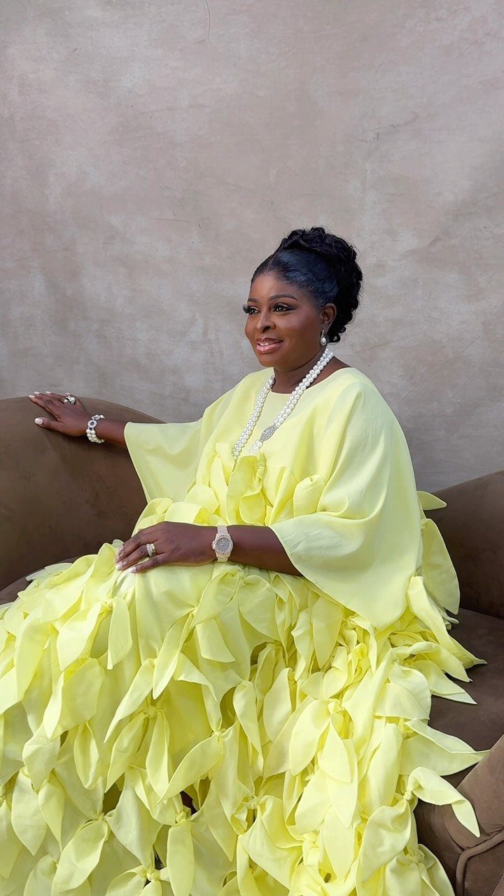 Woman in a voluminous yellow ruffled gown and pearl necklace sitting on a sofa.