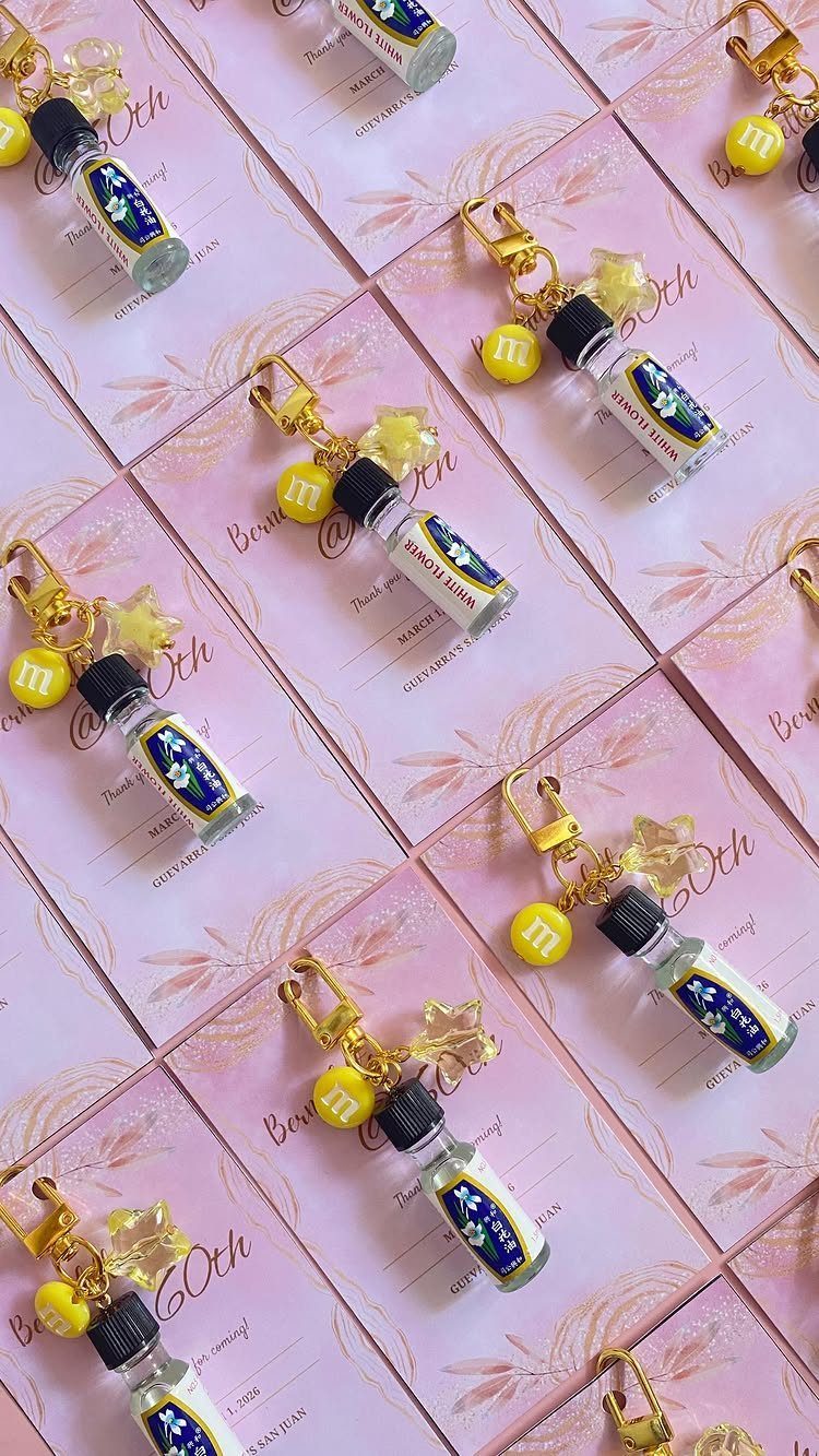 Pink 60th birthday invitations paired with small decorative glass vials and gold clasps.