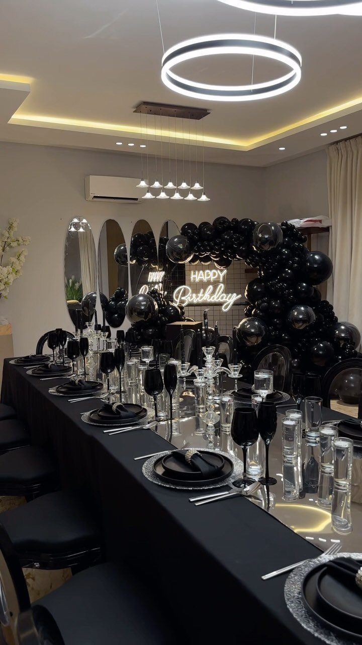 Elegant black birthday dinner table setting with a black balloon arch and neon sign.