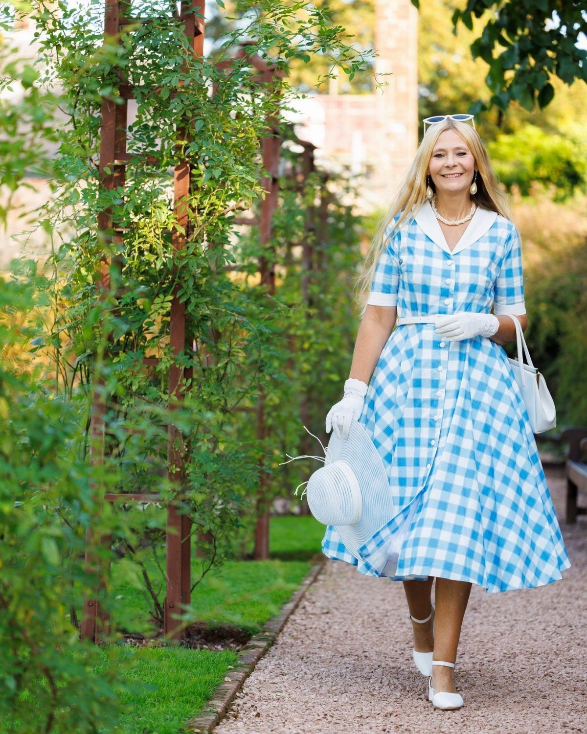 Blonde woman in a blue and white gingham midi dress walking in a garden