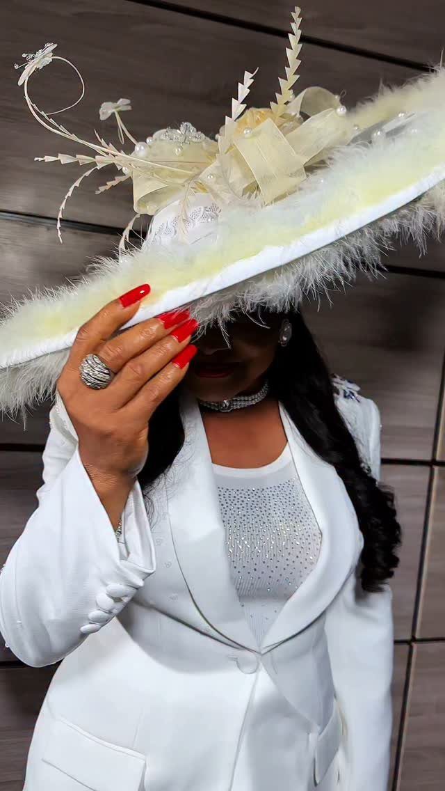 Woman in an all-white tailored suit and large ornate feathered hat.