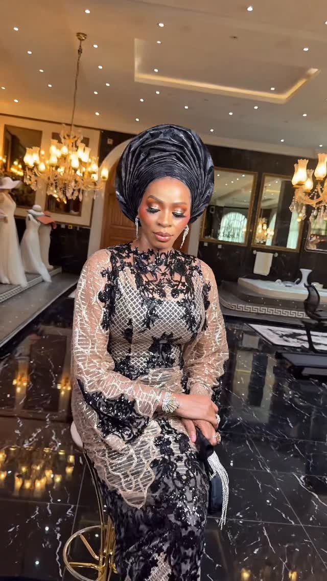 Woman in a black and gold lace dress with a black gele headtie.