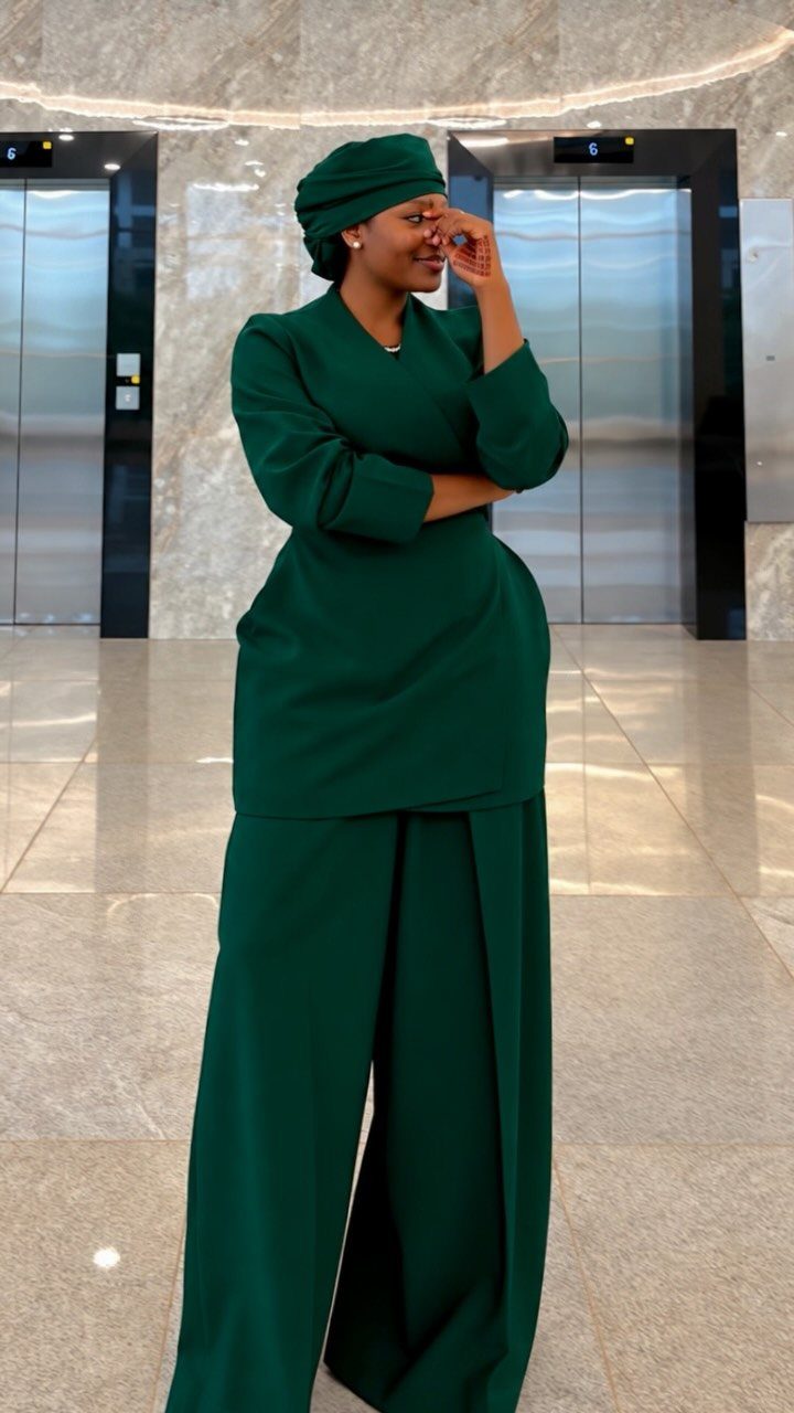 Woman in a dark green tunic, wide-leg trousers, and matching headwrap in a lobby.