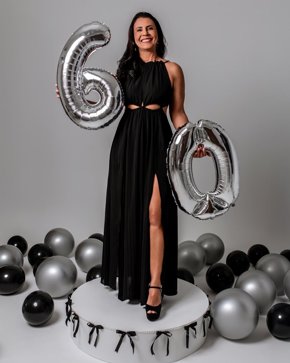 Woman in black maxi dress holding silver 60 balloons among black and silver balloons