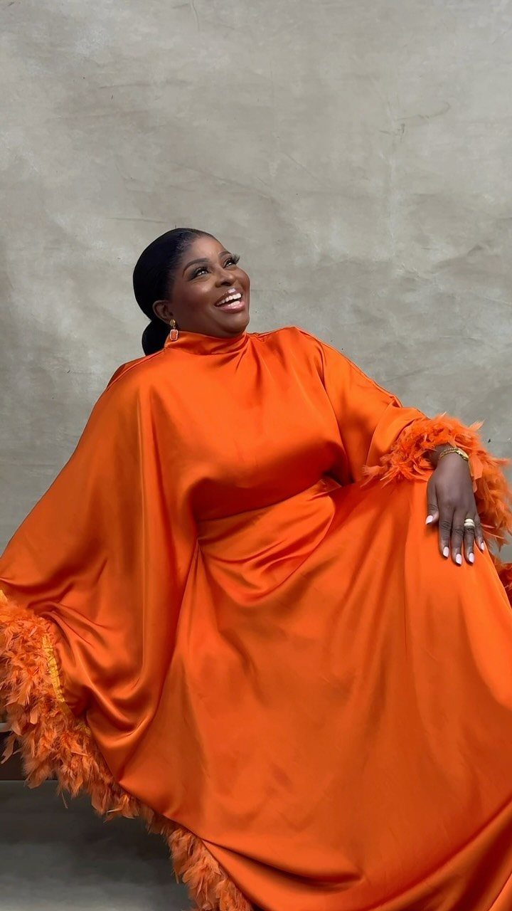 Woman in a voluminous orange satin gown with feather trim posing and smiling.
