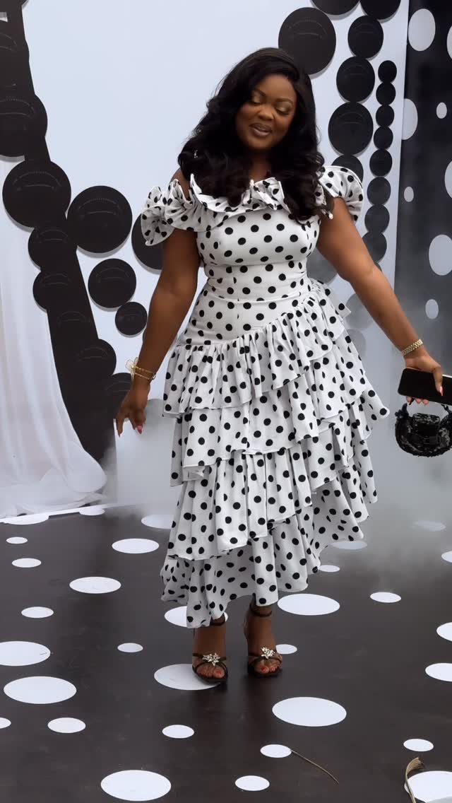 Woman wearing a white and black polka dot midi dress with tiered ruffles.