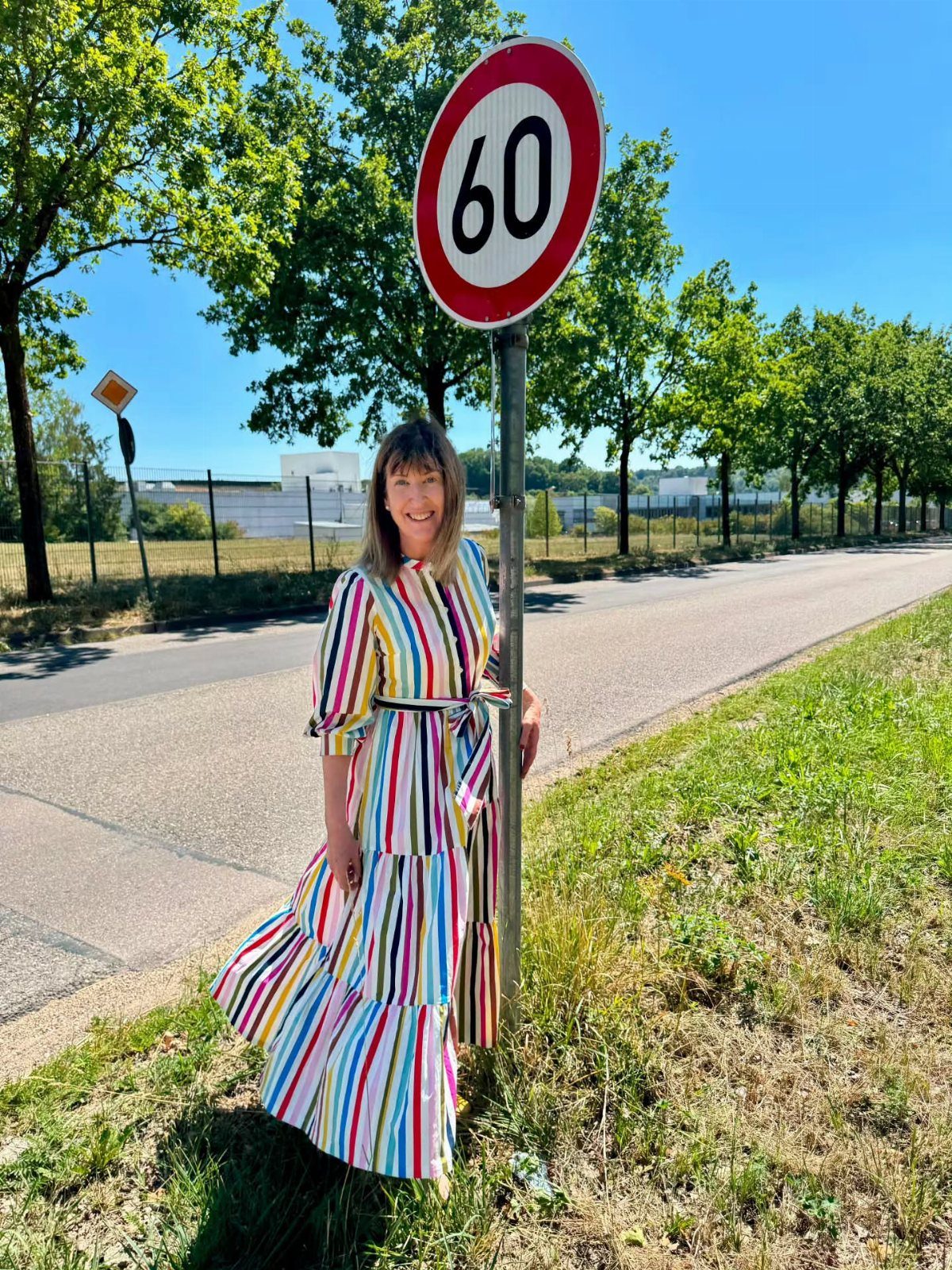 Woman in a colorful striped maxi dress standing beside a 60 speed limit sign.