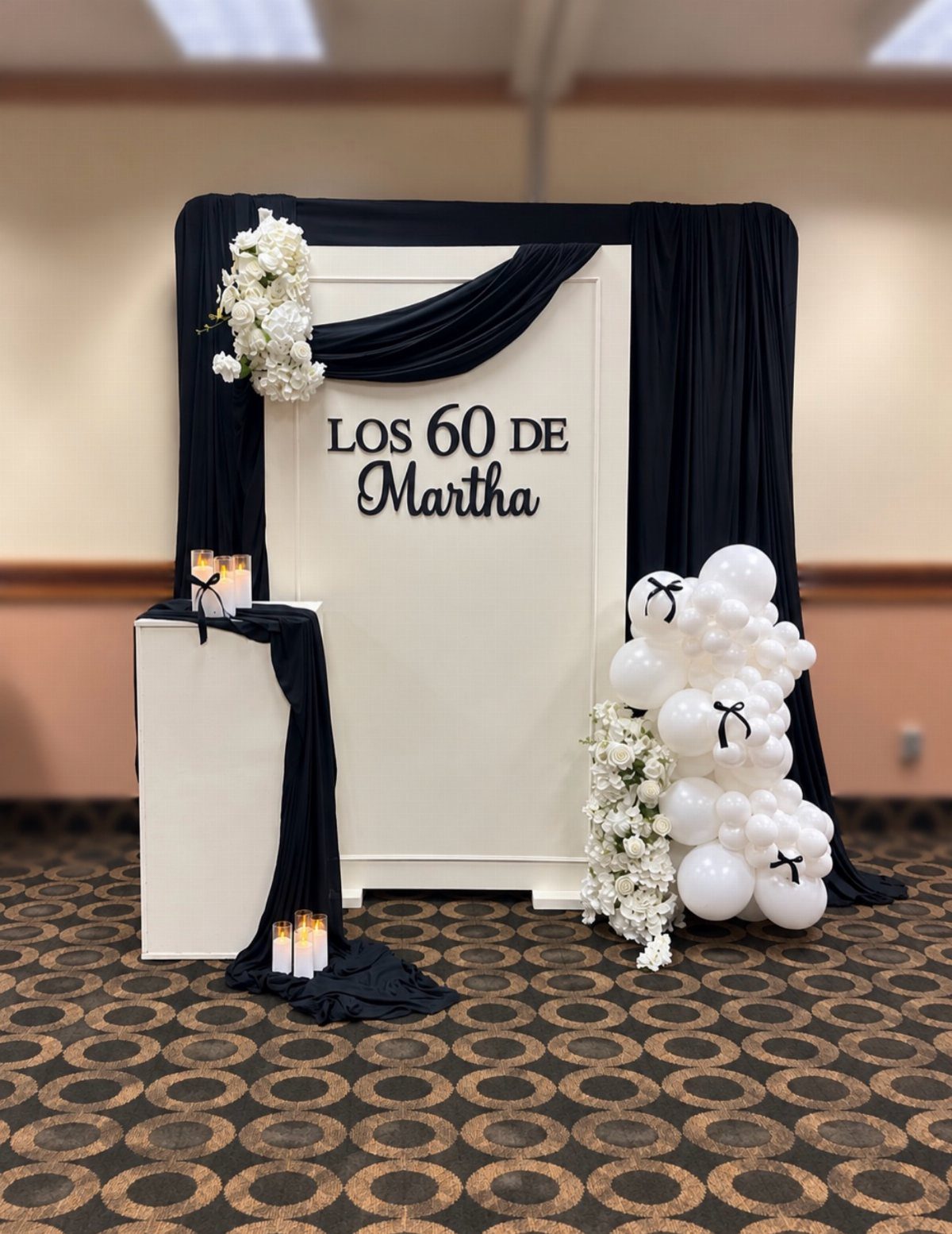 Black and white party backdrop with balloons, flowers, and 60th birthday text.