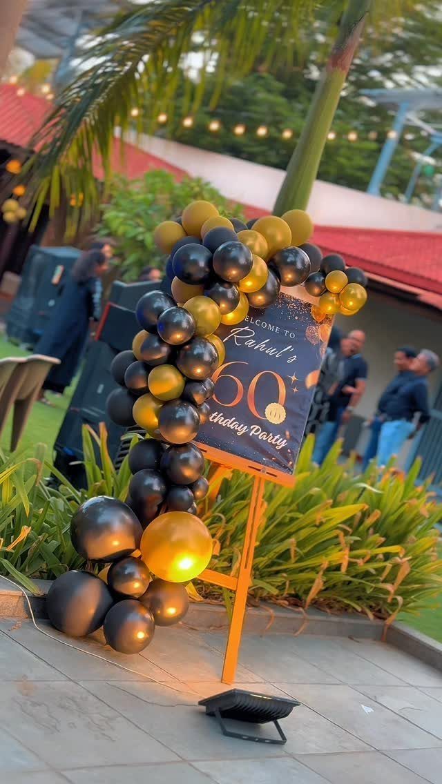 Black and gold balloon arch framing a 60th birthday welcome sign outdoors.