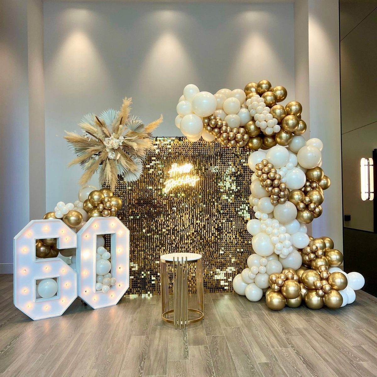 Illuminated number 60 with gold sequin backdrop and white and gold balloons.
