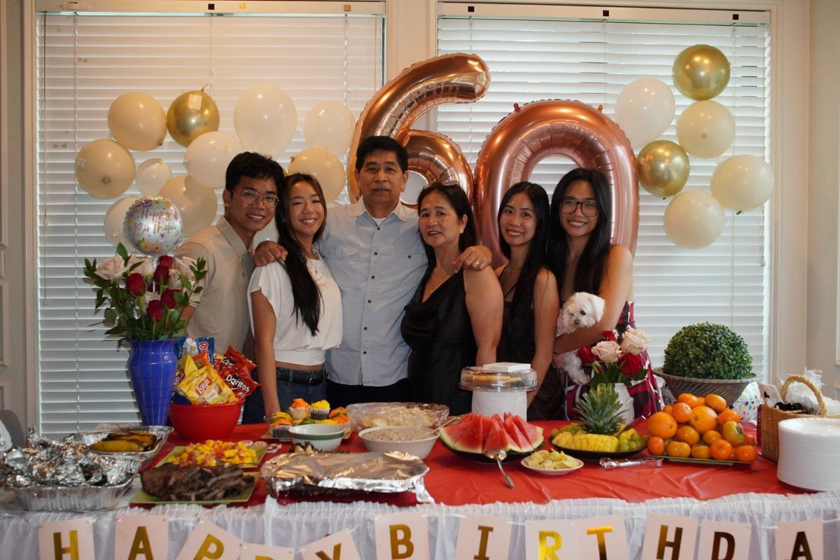 Family posing behind a birthday food table with 60 balloons and banner.