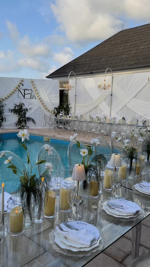 Elegant outdoor party table with white flowers and candles beside a swimming pool