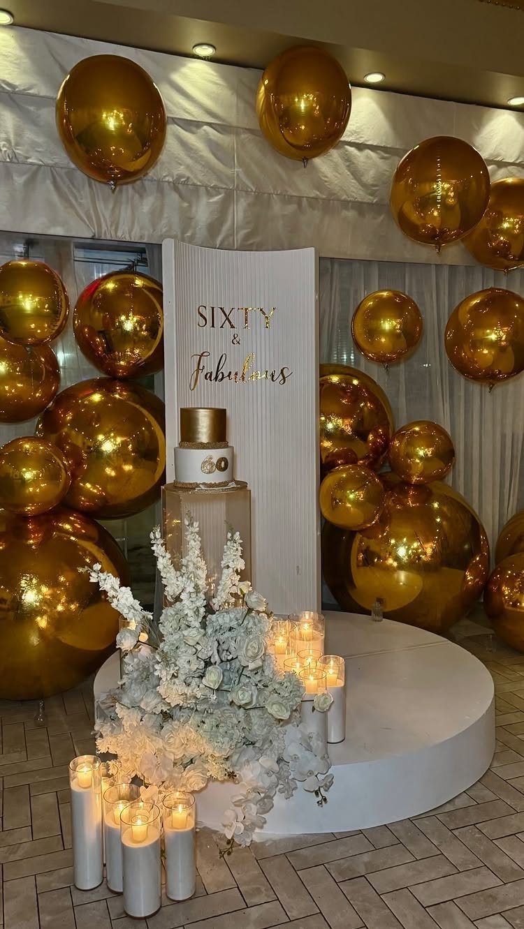 Gold balloons and white floral decor with a Sixty and Fabulous backdrop.