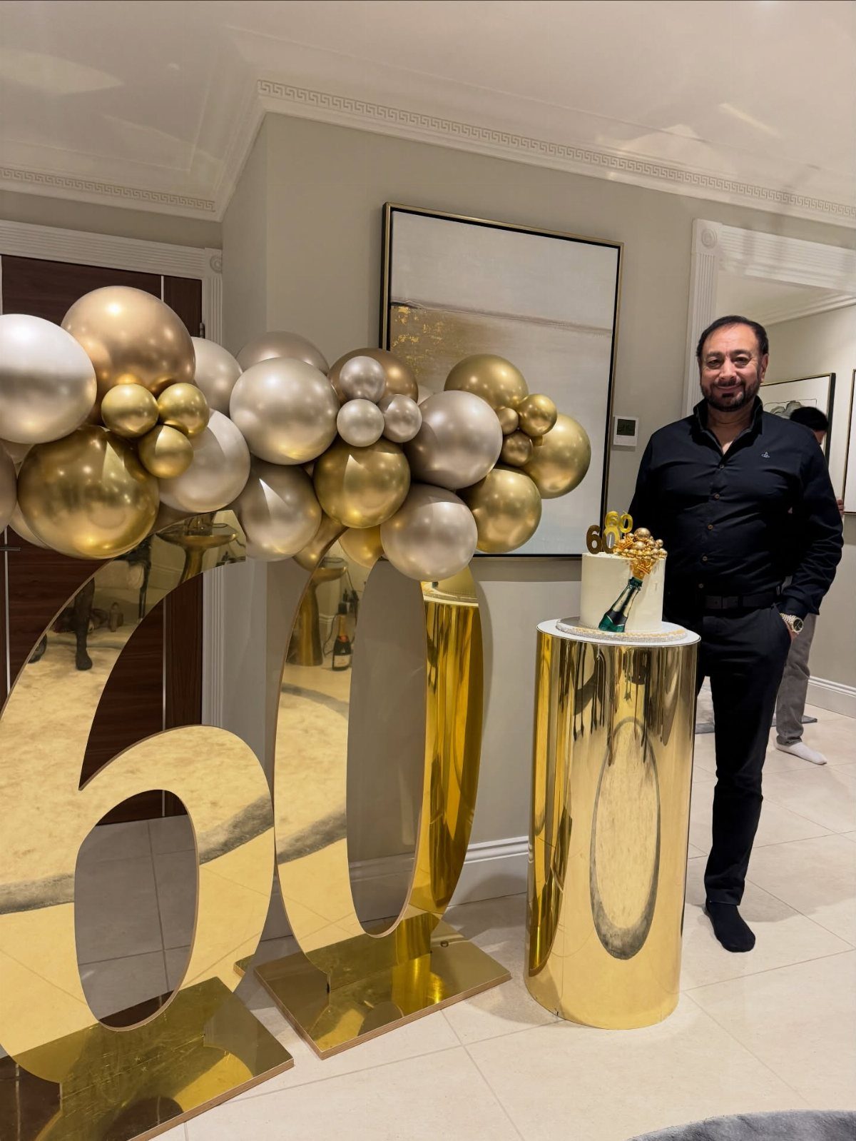 Man standing by large gold mirrored 60 numbers and gold and silver balloons.