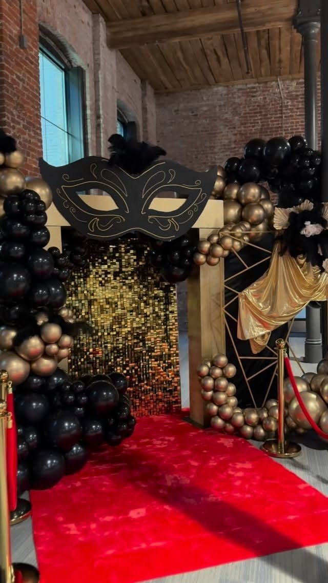 Red carpet entrance with black and gold balloons and a large masquerade mask.