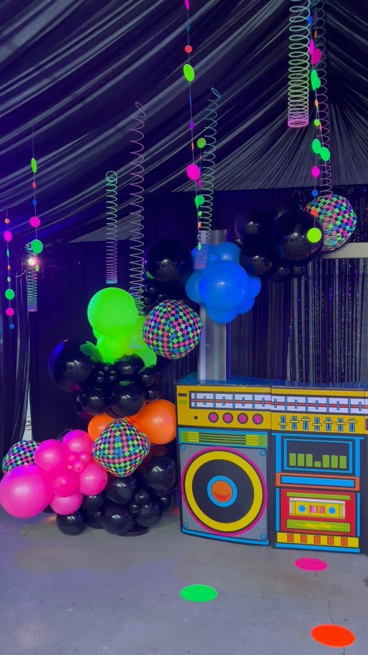 Neon balloons and a colorful DJ booth against a black draped background.