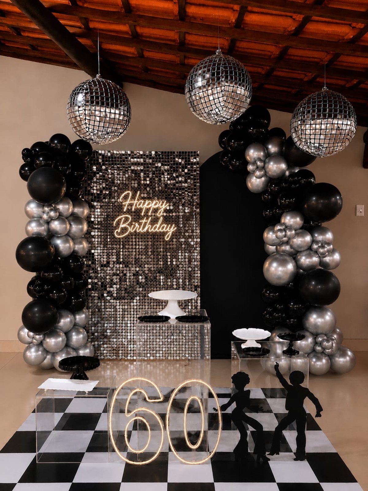 Silver and black birthday decorations with disco balls and a glowing number 60 sign.
