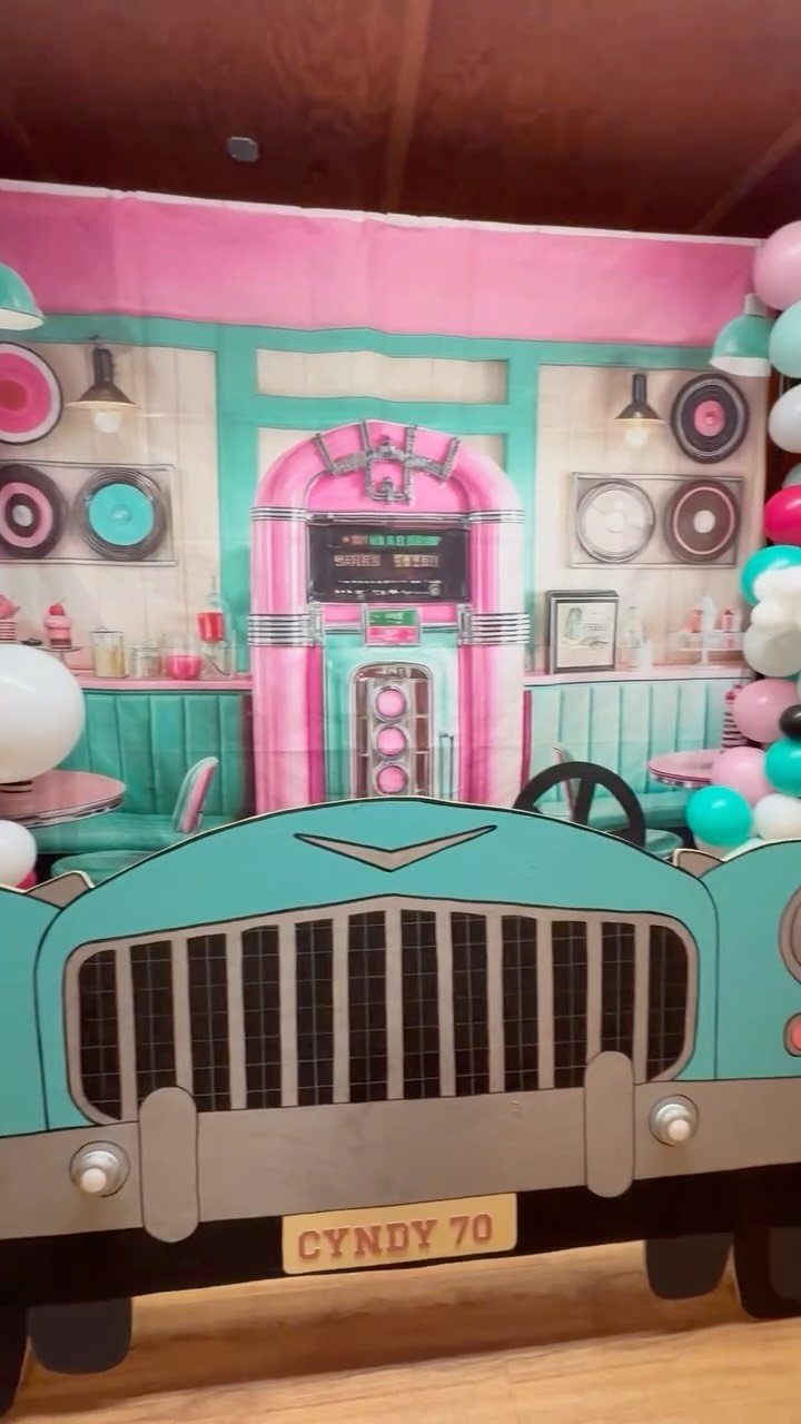 Vintage 1950s diner party decorations with a teal car cutout and pink backdrop.