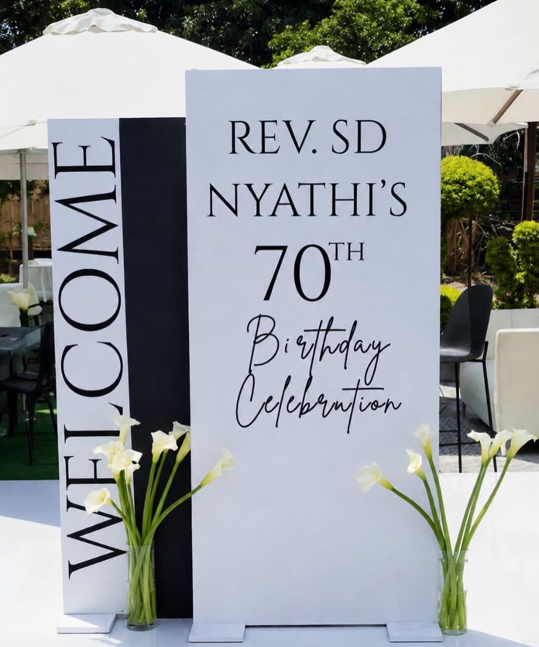 Black and white 70th birthday welcome sign with white calla lilies outdoors