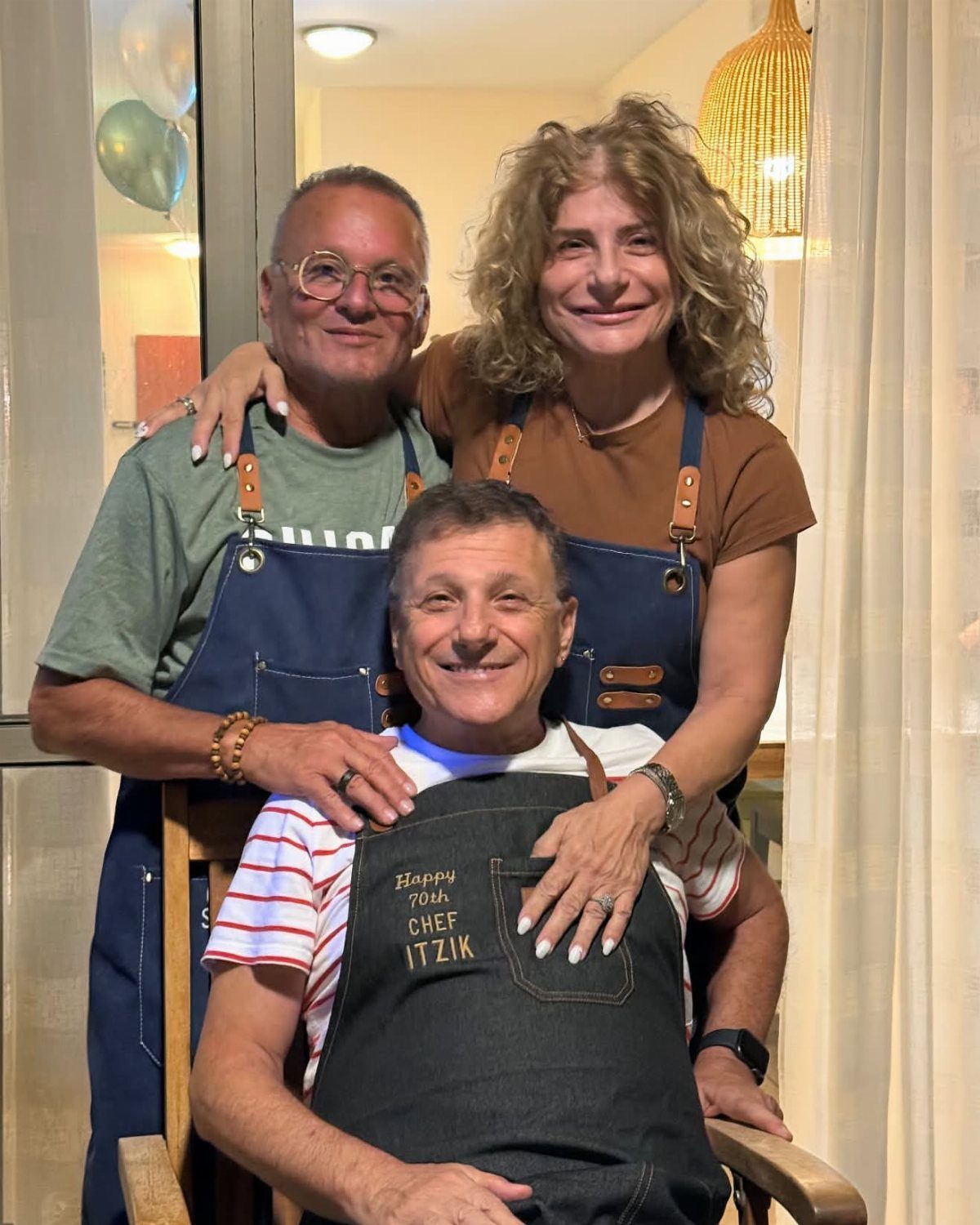 Three adults wearing aprons, with the center man's apron celebrating his 70th birthday.