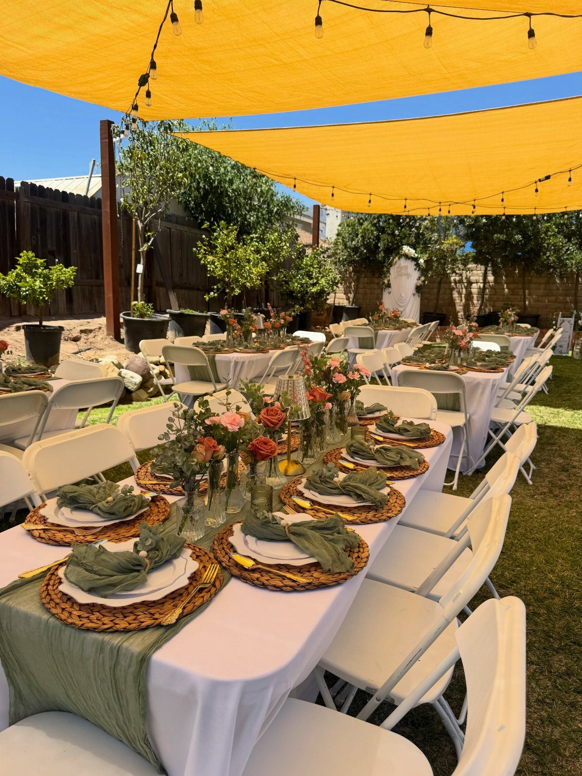 Elegant outdoor dining table with floral centerpieces under yellow sun sails in a garden