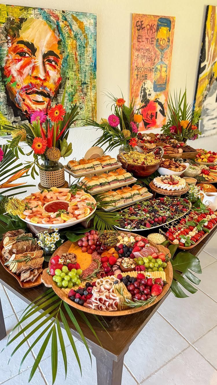 Lavish party food spread on a wooden table with colorful floral arrangements.
