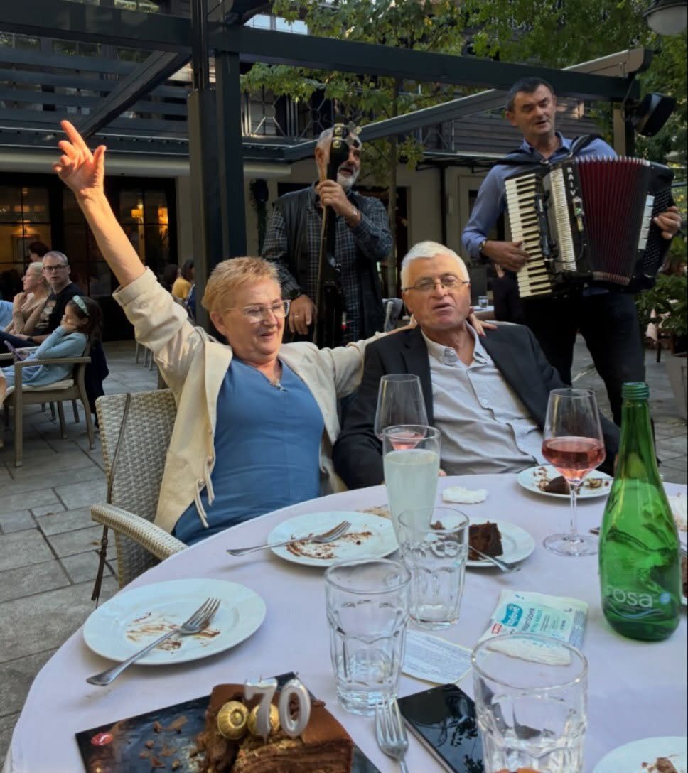 Older couple celebrating 70th birthday at outdoor table with musicians playing in background