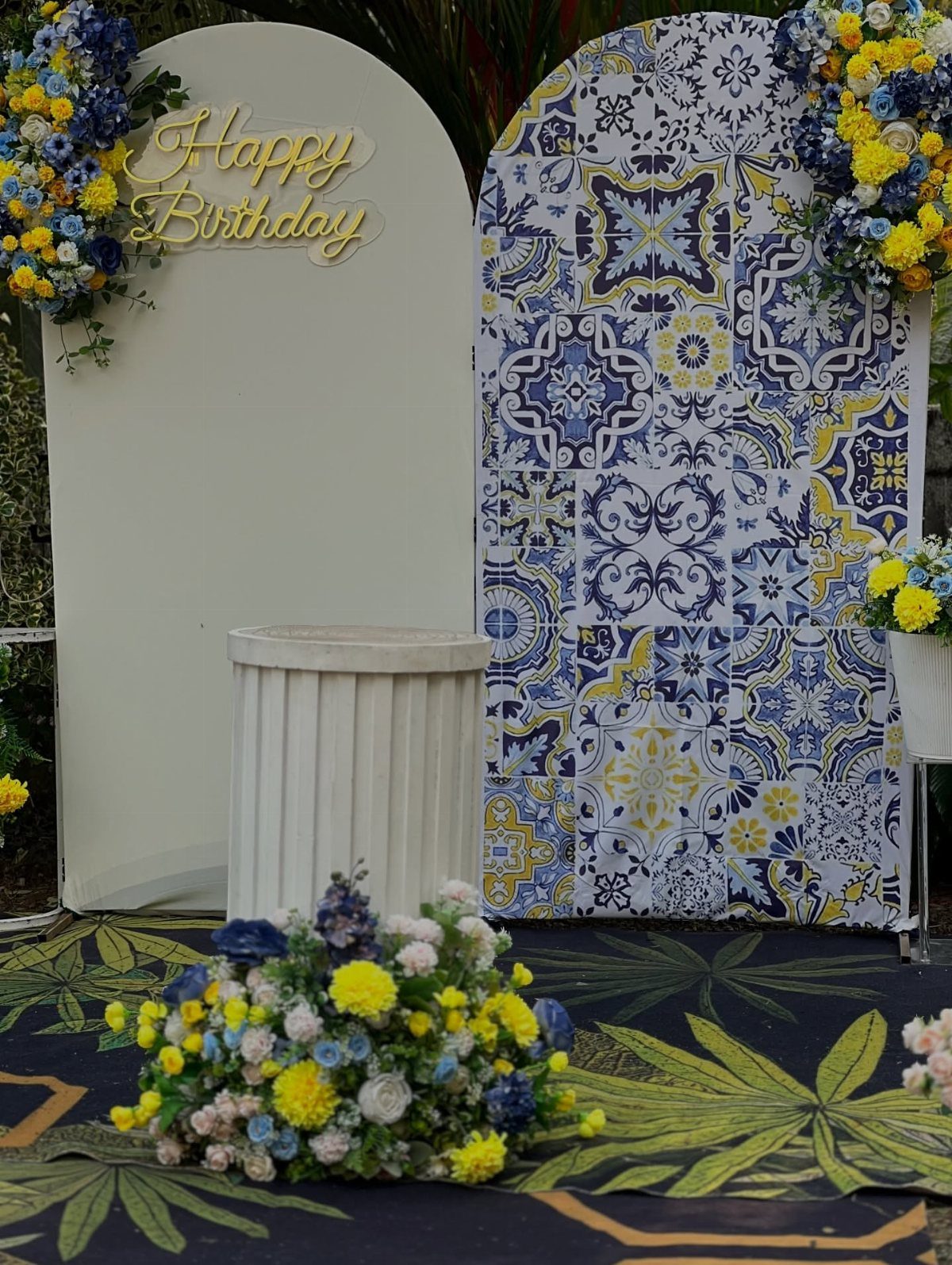 Birthday party backdrop with blue and yellow flowers and patterned tile panel.