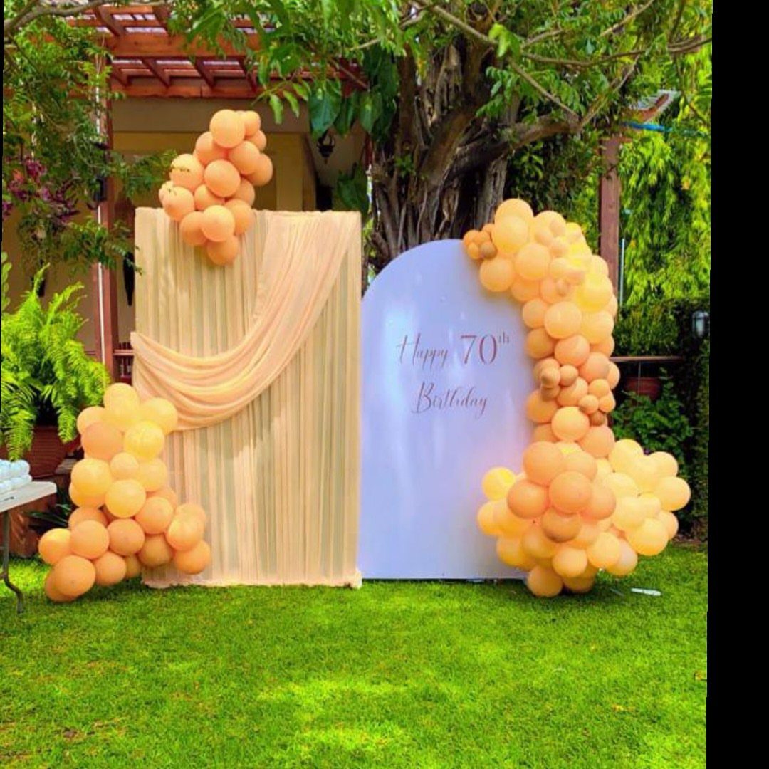 Birthday photo booth backdrop with peach balloons and Happy 70th Birthday text outdoors