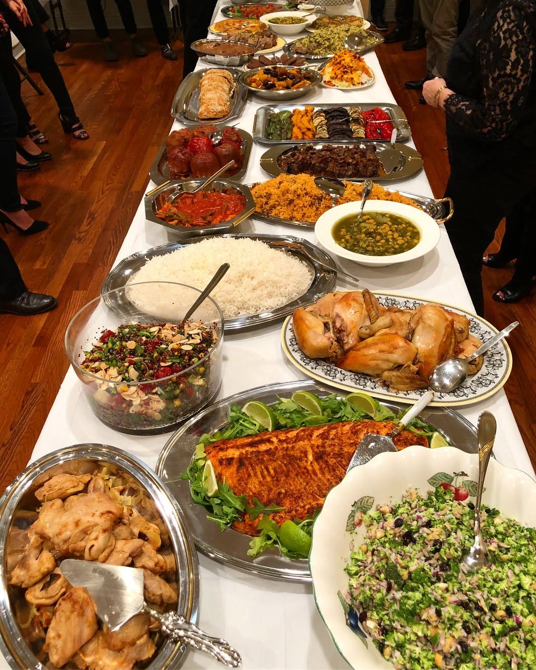 Long white table filled with diverse food platters and bowls for a gathering.